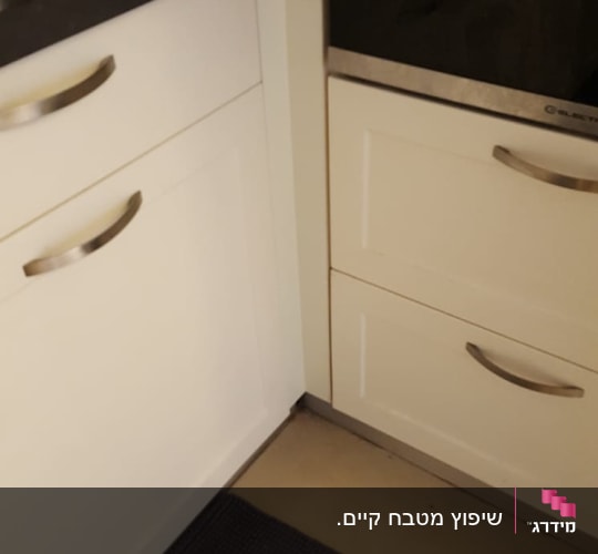 ארונות מטבח לבנים עם ידיות מתכת, בקבוק שמן על השיש